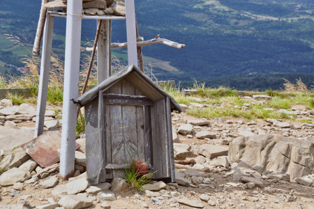 Wooden structure in the shape of a cottage, memory, tombstone with a candle, supported by a metal steel structure in the mountains, rocky ground, mountains in the background, Bieszczady National Parkの写真素材