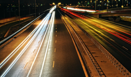 This captivating night photography utilizes a long exposure technique to transform moving vehicles into vibrant streaks of light. The image captures cars traveling in both directions on a highway, with red taillights and white headlights creating dynamic lines across the frame. The blurring effect emphasizes speed and motion, highlighting the constant flow of urban life after dark. Ideal for themes related to urban transport, night photography, speed, cityscapes, and the abstract beauty of light trails.の写真素材