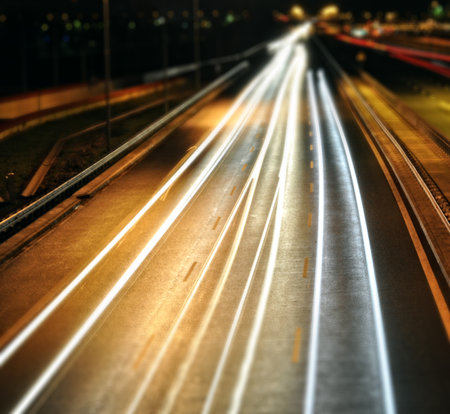 This captivating night photography utilizes a long exposure technique to transform moving vehicles into vibrant streaks of light. The image captures cars traveling in both directions on a highway, with red taillights and white headlights creating dynamic lines across the frame. The blurring effect emphasizes speed and motion, highlighting the constant flow of urban life after dark. Ideal for themes related to urban transport, night photography, speed, cityscapes, and the abstract beauty of light trails.の写真素材