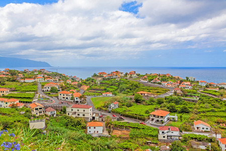 Ponta Delgada, Madeira - June 7, 2013: View over town Ponta Delgada, north coast of Madeira - typical small houses with orange roofs in green nature - the Atlantic Ocean in the background.のeditorial素材