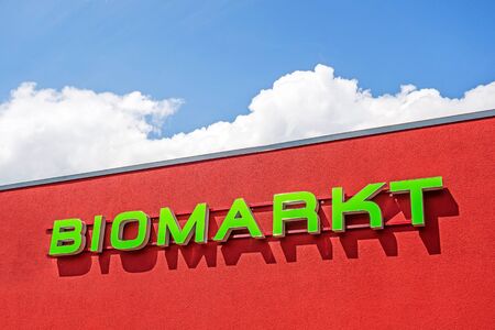 Bio market red facade labeled with "BIOMARKT", german language, blue sky with cloudsのeditorial素材