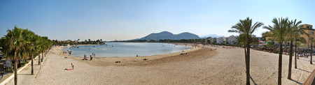 Alcudia, Majorca, Spain - June 26, 2008: Beach panorama of Alcudia with hotels on the right and promenade with palms on the left.の写真素材