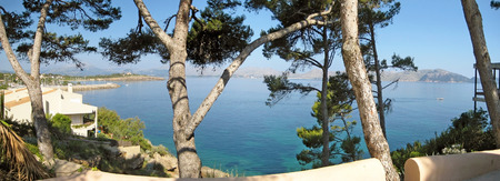 Bay of Pollenca, houses at coast - view through trees towards peninsula Formentor, Majorca, Spainの写真素材