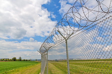 fence with barbed wire, green landscape and blue sky with cloudsの写真素材