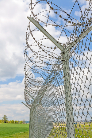 fence with barbed wire, green landscape and blue sky with cloudsの写真素材