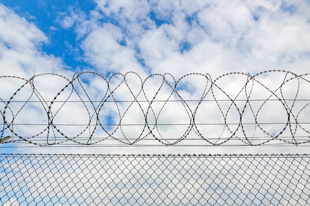 fence with barbed wire against blue sky with cloudsの写真素材