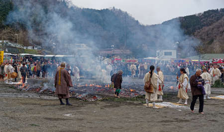 An old woman crosses the fire-walking space as monks and a large crowd watch at the annual fire-walking festival near Mount Takao, west of Tokyoのeditorial素材