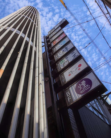 Osaka, Japan - November 5 2020: Daytime view looking up from the base of a tall narrow building full of bars and restaurants in central Osaka on a partly cloudy dayのeditorial素材