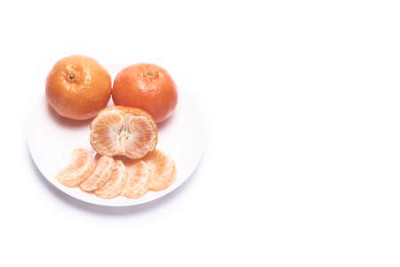Whole, peeled tangerines on a white plate with space for text on a white backgroundの写真素材