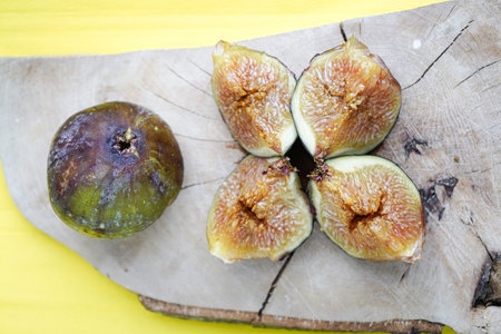 Fresh figs on a wooden cutting board on a yellow background.