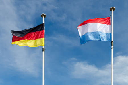 A germany and luxembourg flags are floating in a blue skyの写真素材