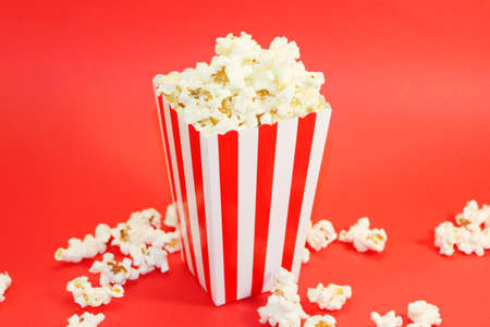 A bucket with popcorn sitting on top of a table. High quality photo. Basket with popcorn on a red background. Popcorn on a red background with place for text. Watching a movie with popcornの写真素材