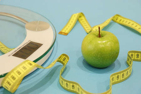 Healthy lifestyle. Layout on the topic of healthy eating. Bathroom scales and an apple on a blue background. The concept of a healthy diet, body weight controlの写真素材