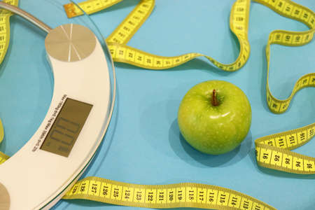 Healthy lifestyle. Layout on the topic of healthy eating. Bathroom scales and an apple on a blue...