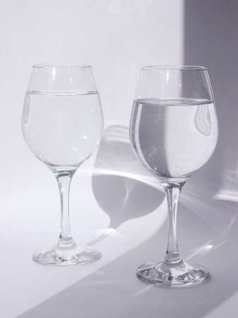 Glass with water on a white background. The play of shadow and light. Summer white background. High quality photoの写真素材