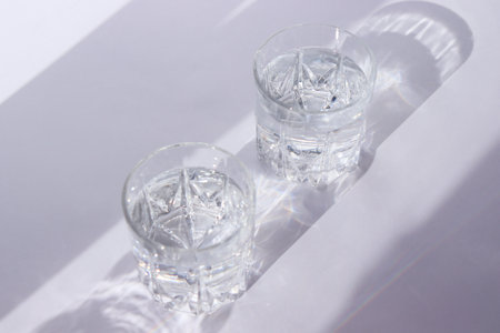 Glass with water on a white background. The play of shadow and light. Summer white background. High quality photoの写真素材