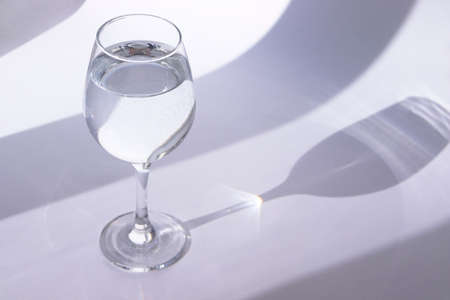 Glass with water on a white background. The play of shadow and light. Summer white background. High quality photoの写真素材