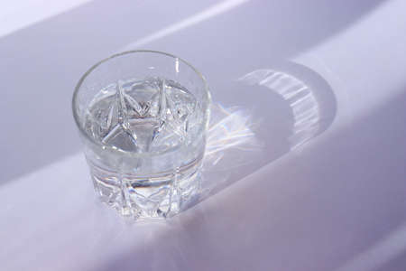 Glass with water on a white background. The play of shadow and light. Summer white background. High quality photoの写真素材