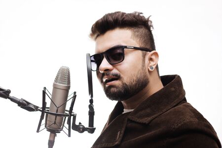Talented young man wearing a brown and glasses coat singing a song in studio recording