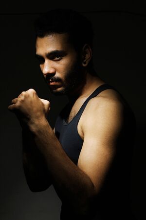 Confident Young Fitness Man With Strong Hands And Clenched Fists In Dark Dramatic Light
