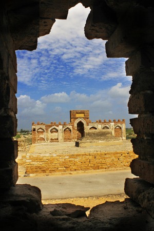 A beautiful view of tomb from a hole in a wall with some blue skys and clouds in makli grave yard, Sindh, Pakistanの写真素材