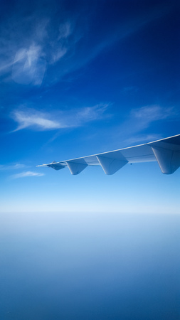 Plane wing against the beautiful blue sky and clouds and ocean from the window of plane - Vertical Photoの写真素材