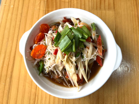 Papaya salad with chicken and vegetables in a white bowl.
