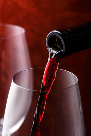 Pouring red wine into the glass against a wooden backgroundの写真素材