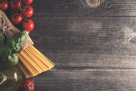 Spaghetti, tomatoes, olive oil, fresh basil herb on an old wooden table. Place for your text. Top view.の写真素材