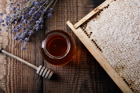 Honey in a glass jar, honeycombs, honey spoon, lavender flowers on an old wooden table. Dark background. Top view.の写真素材