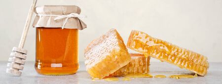 Honey background. Sweet honey in the comb, glass jar and a spoon for honey on the table. Light background.の写真素材