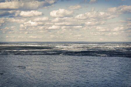 Spring melting ice on the river. Against the background of blue sky and clouds. River landscape in...