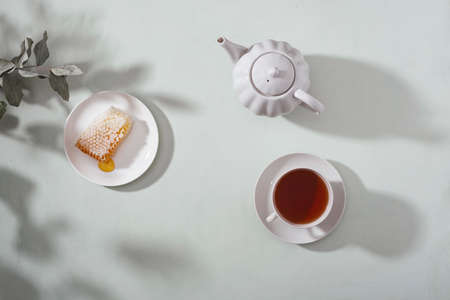 Fresh tea in a ceramic cup and teapot, honeycomb on the table. Light background. Top view.