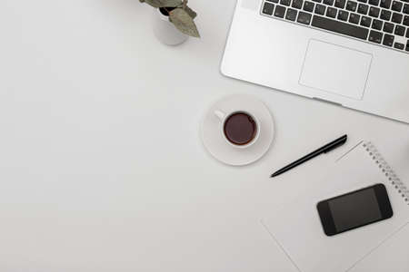 Desk office with laptop, blank notepad, coffee cup and pen on white table. Flat lay top view copy space.の写真素材