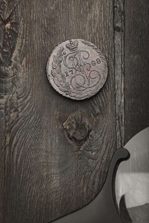 Numismatics. Antique collectible coin and magnifier on an old wooden table. Dark background. Top view.の写真素材