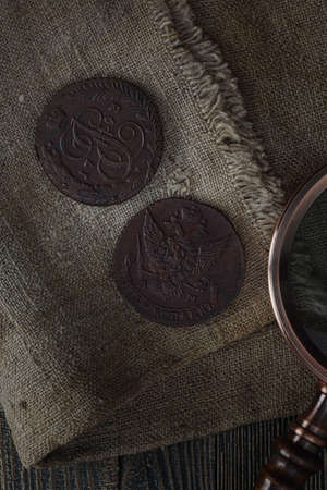 Numismatics. Old collectible coins and a magnifying glass on a wooden table. Dark background. Top view.の写真素材