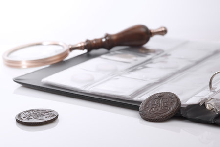 Numismatics. Old collectible coins and a magnifying glass on the table. Light background.の写真素材