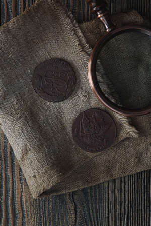 Numismatics. Old collectible coins and a magnifying glass on a wooden table. Dark background. Top...