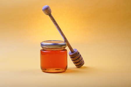 Honey background. Sweet honey in the comb, glass jar and a spoon for honey on the table. Light...