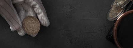 Numismatics. Old collectible coins of silver, gold and copper on the table. A collector in special gloves holds an old coin. top view. Banner.の写真素材