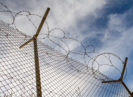 Metal mesh fence with barbed wire against a background the cloudy sky