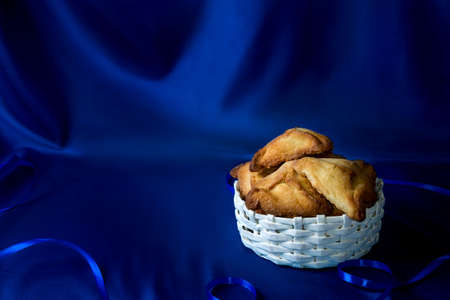 Hamantaschen or Haman's ears - triangular cookies for Jewish holiday of Purim on dark blue silk...
