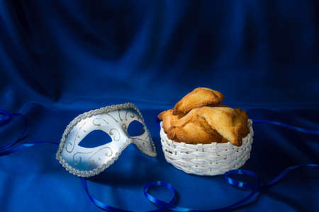 Jewish holiday of Purim. Hamantaschen cookies and carnival mask on dark blue silk background