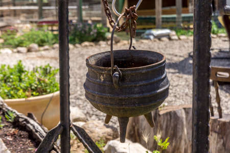 Old cast iron pot on a three legs for cooking is suspended on the hook, on the farm in the desert, Israelの写真素材