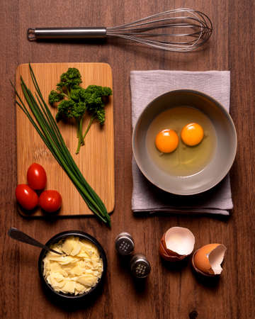 preparation to make an omelet, with eggs, cheese, salt, black pepper, tomates, green onions and parsley on a wooden background.の写真素材