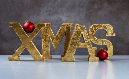 golden XMAS letters on white table and gray background with red Christmas ballsの写真素材