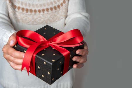 Woman holding gift in her hands. Red bow. Gray background. Christmas or Valentine's Day. Front view, copy space.の写真素材