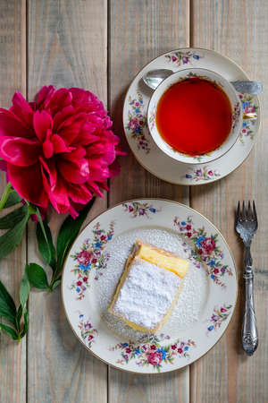 Slice of vanilla cake and a cup of tea on a gray table and a red flower, top view.の写真素材