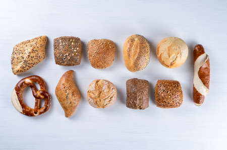 various delicious, freshly baked rolls individually on a white table, top view.