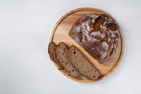 Freshly baked rye bread sliced in the traditional way. Single object on a wooden plate on a white table. Top view, copy space.の写真素材